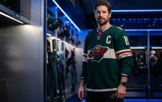 Confident Minnesota athlete with full hair standing in a hockey locker room, representing hair transplant recovery for athletes.
