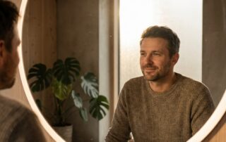 Man examining hair transplant results at 6 months in mirror, looking optimistic about continued growth progress